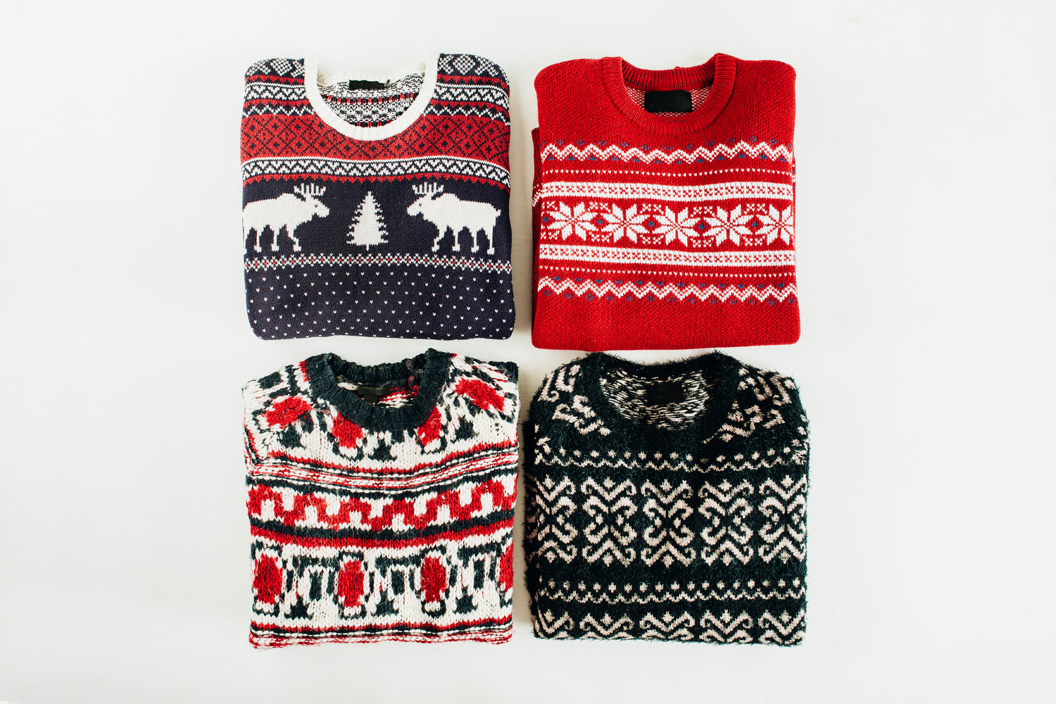 Four Christmas-themed sweaters with reindeer and snowflake patterns on a white background.